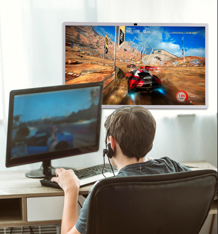 a gamer playing a racing game on a computer monitor while simultaneously displaying the game on a wall-mounted sidek itv smart display. the setup provides an immersive gaming experience with a larger secondary screen for enhanced visuals.